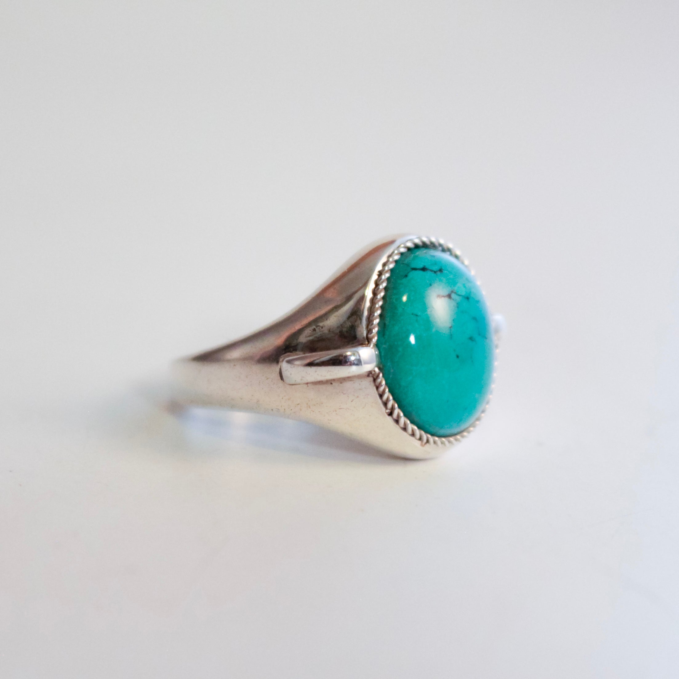 A sterling silver signet ring featuring a large, oval Hubei Turquoise cabochon stone in a bezel setting with a twisted rope border, photographed on a plain white background.