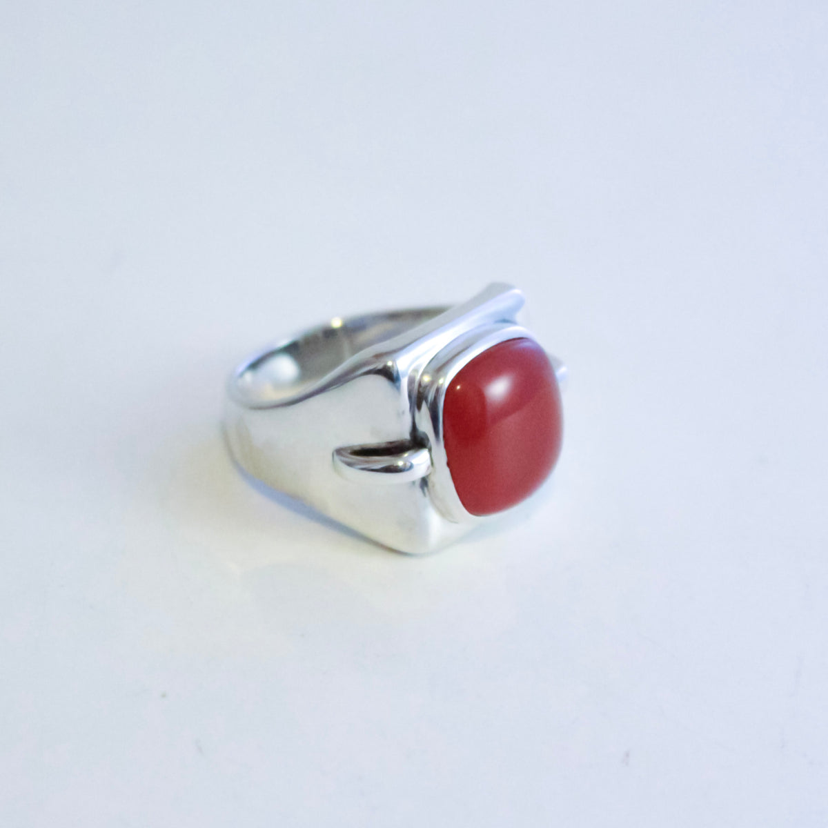 A sterling silver ring with a curved, sculptural band and a smooth, oval red agate cabochon gemstone, shown on a plain white background.