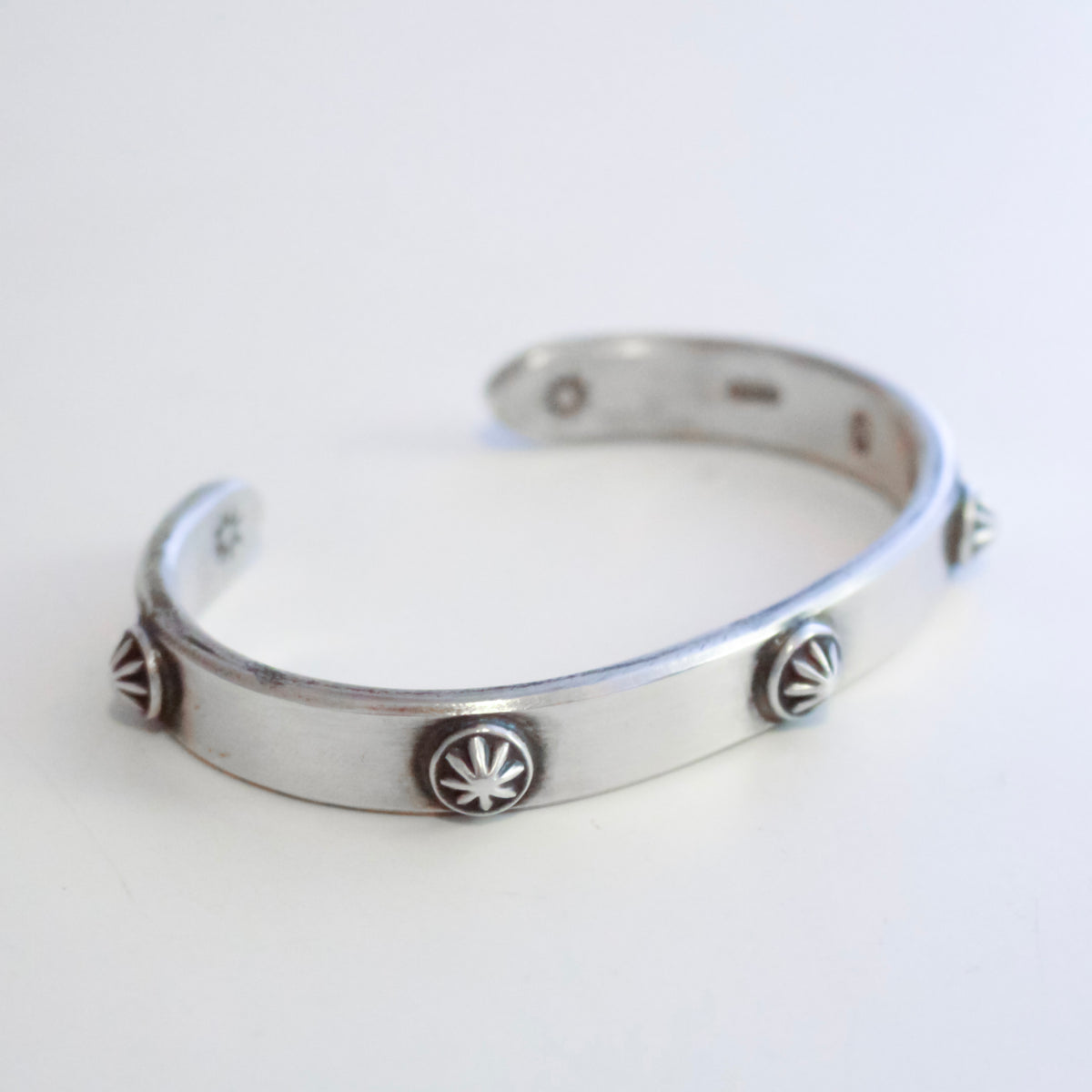 A silver-toned open cuff bracelet with five decorative starburst medallions spaced along the front, photographed on a plain light background.