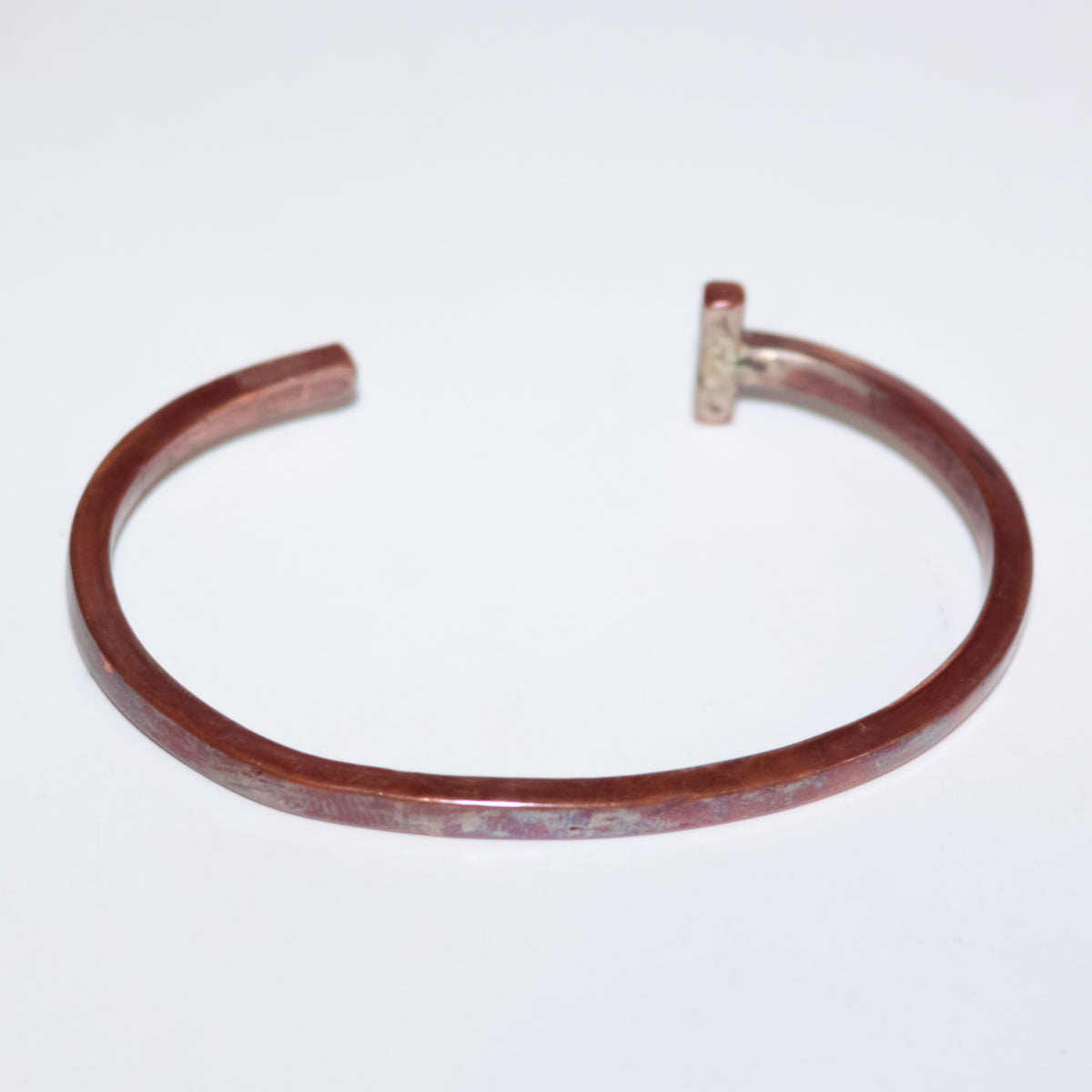 A hammered copper-toned open cuff with a small rectangular accent at the open end, shown on a plain white background.