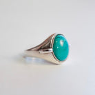 A sterling silver signet ring featuring a large, oval Hubei Turquoise cabochon stone in a bezel setting with a twisted rope border, photographed on a plain white background.