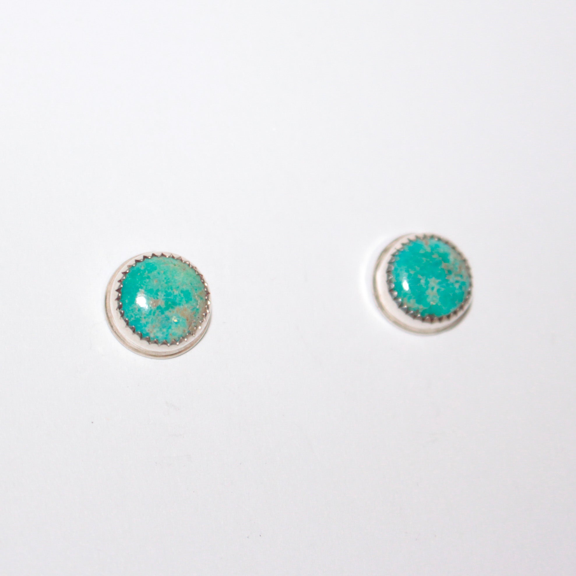 A pair of round stud earrings with turquoise stones set in silver, shown on a plain white background.