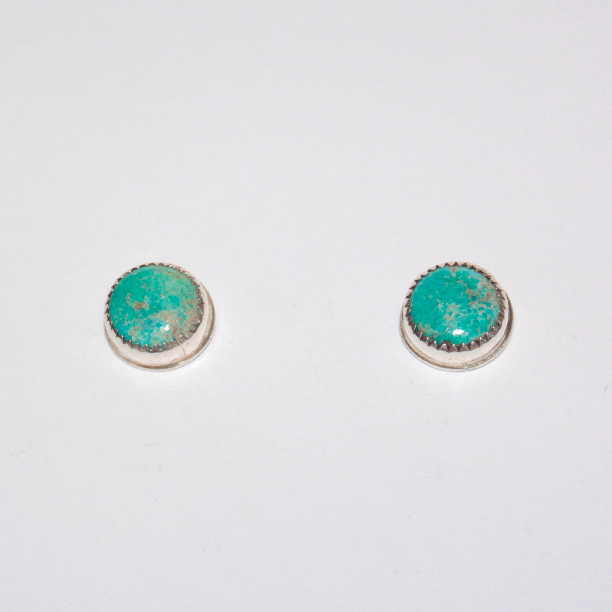 A pair of silver stud earrings with oval turquoise cabochon stones, displayed on a plain white background.