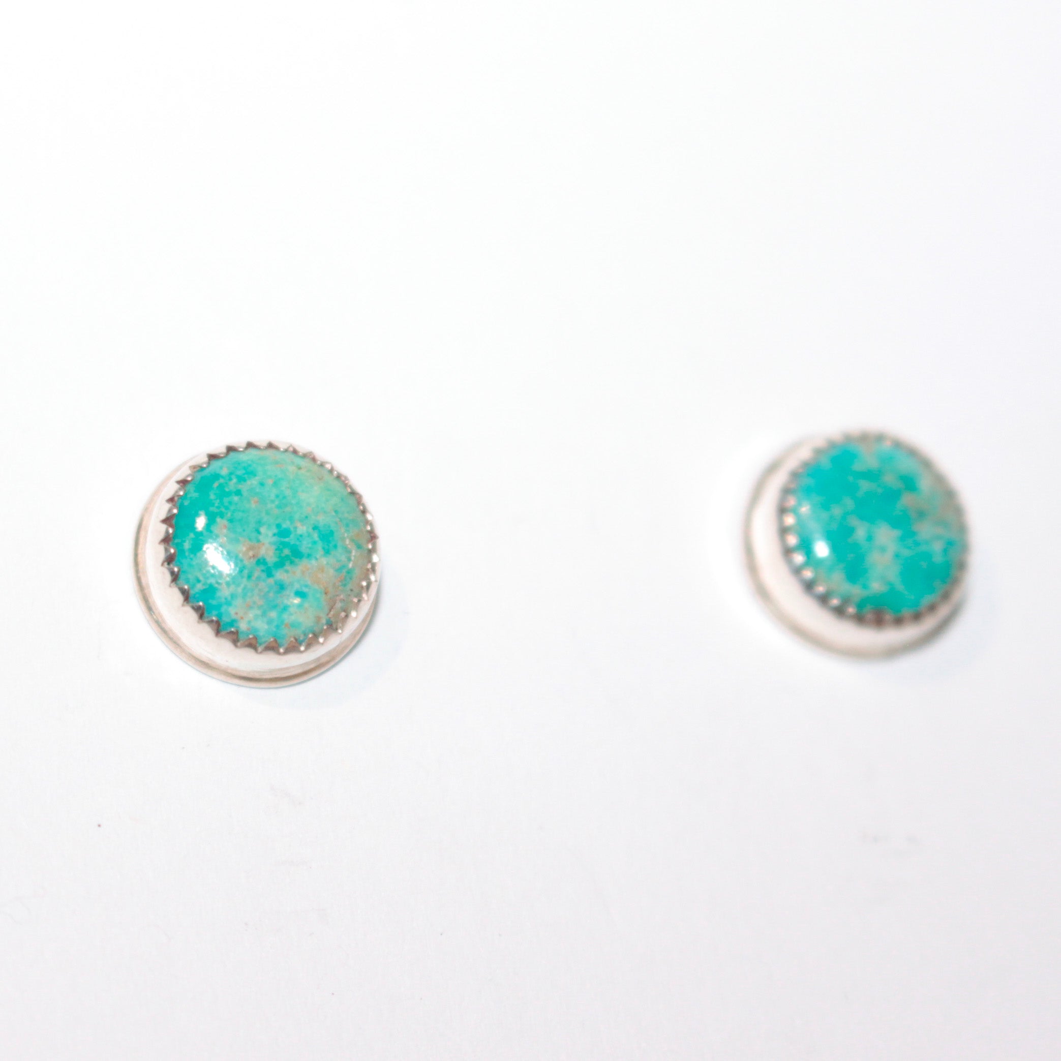 A pair of round stud earrings featuring turquoise stones in silver bezel settings, displayed on a plain white background.