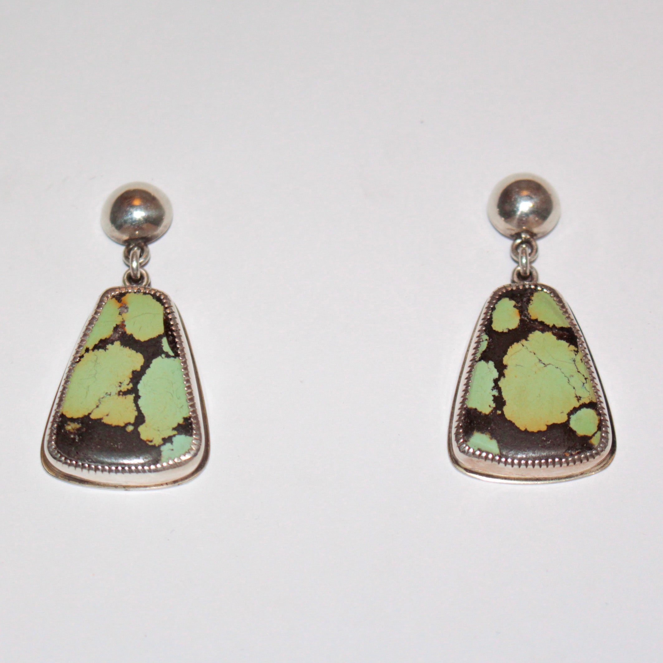 A pair of sterling silver stud earrings featuring irregular triangle-shaped Bao Canyon Turquoise pendants with a dark brown base and light green matrix, set against a plain white background.