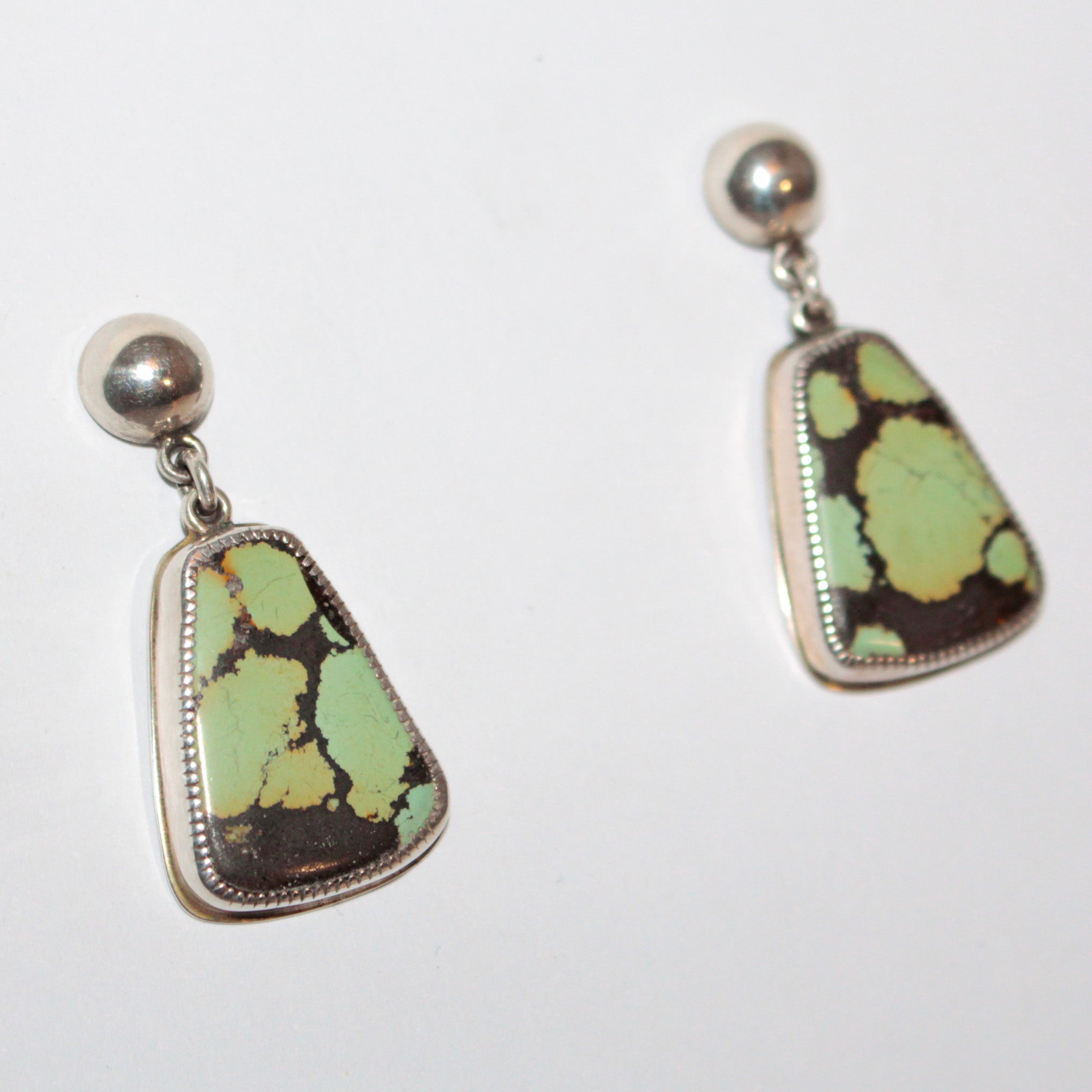 A pair of sterling silver stud earrings featuring irregular, organic-shaped Bao Canyon turquoise stones with a light green and dark brown marbled pattern, set in silver bezel settings with round silver studs.