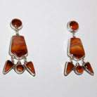 A pair of sterling silver dangle earrings featuring red cherry carnelian stones in various geometric shapes, displayed on a plain white background.

