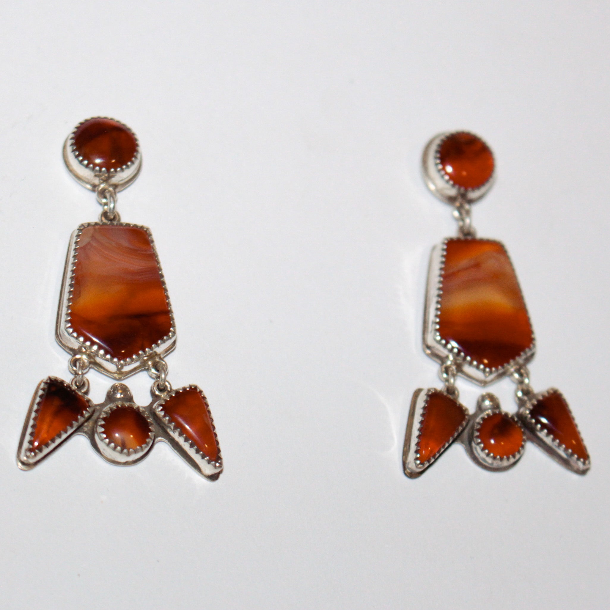 A pair of sterling silver dangle earrings featuring red cherry carnelian stones in various geometric shapes, displayed on a plain white background.


