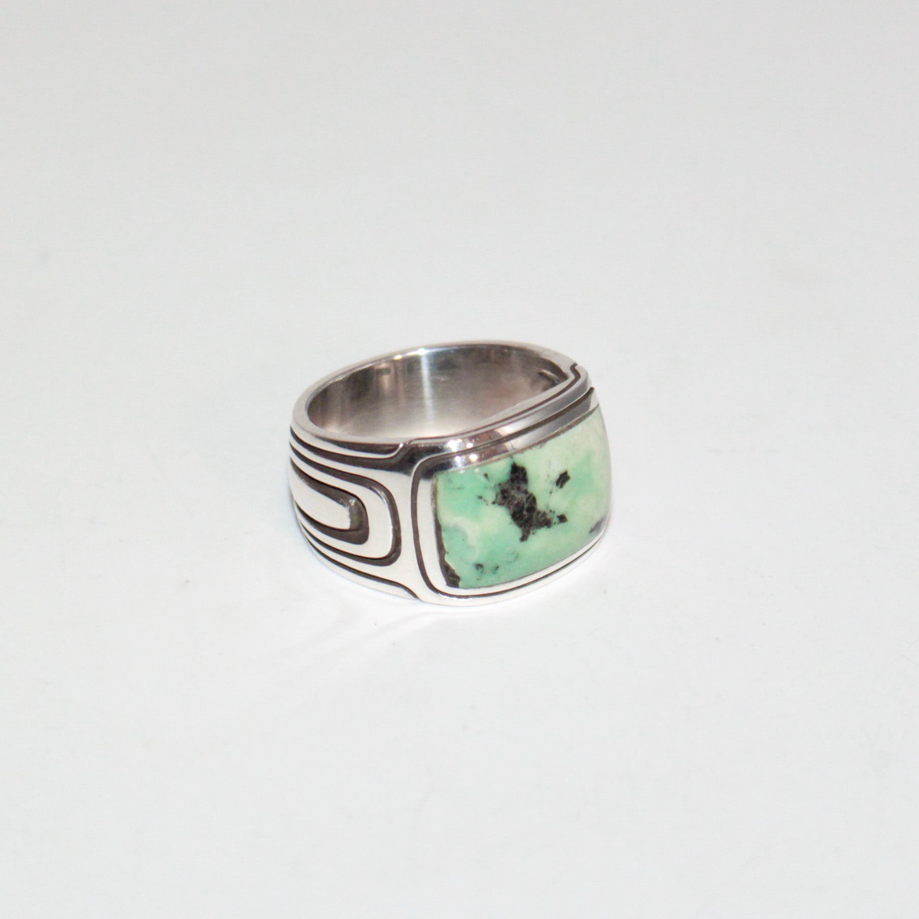 A silver band ring featuring a rectangular green Pixie Turquoise stone with black inclusions, set against a plain white background.