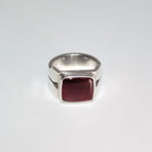 A silver signet-style ring with a square, bezel-set deep burgundy carnelian, photographed on a plain light gray background.