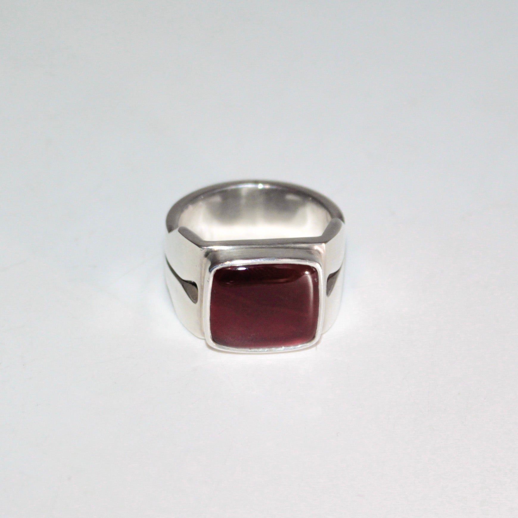 A silver signet-style ring with a square, bezel-set deep burgundy carnelian, photographed on a plain light gray background.