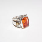 A silver ring featuring a large, square, amber-orange marbled Cherry Carnelian in a bezel setting, with small 22K gold accent bosses on the band, shown on a plain white background.