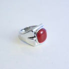 A sterling silver ring with a curved, sculptural band and a smooth, oval red agate cabochon gemstone, shown on a plain white background.