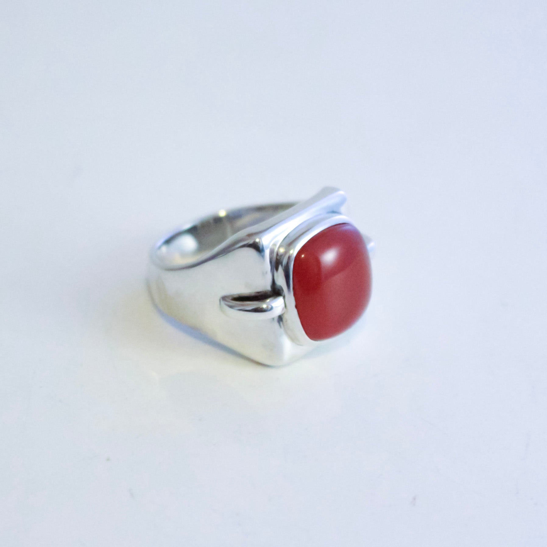 A sterling silver ring with a curved, sculptural band and a smooth, oval red agate cabochon gemstone, shown on a plain white background.