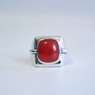 A sterling silver ring with a curved, sculptural band and a smooth, oval red agate cabochon gemstone, shown on a plain white background.