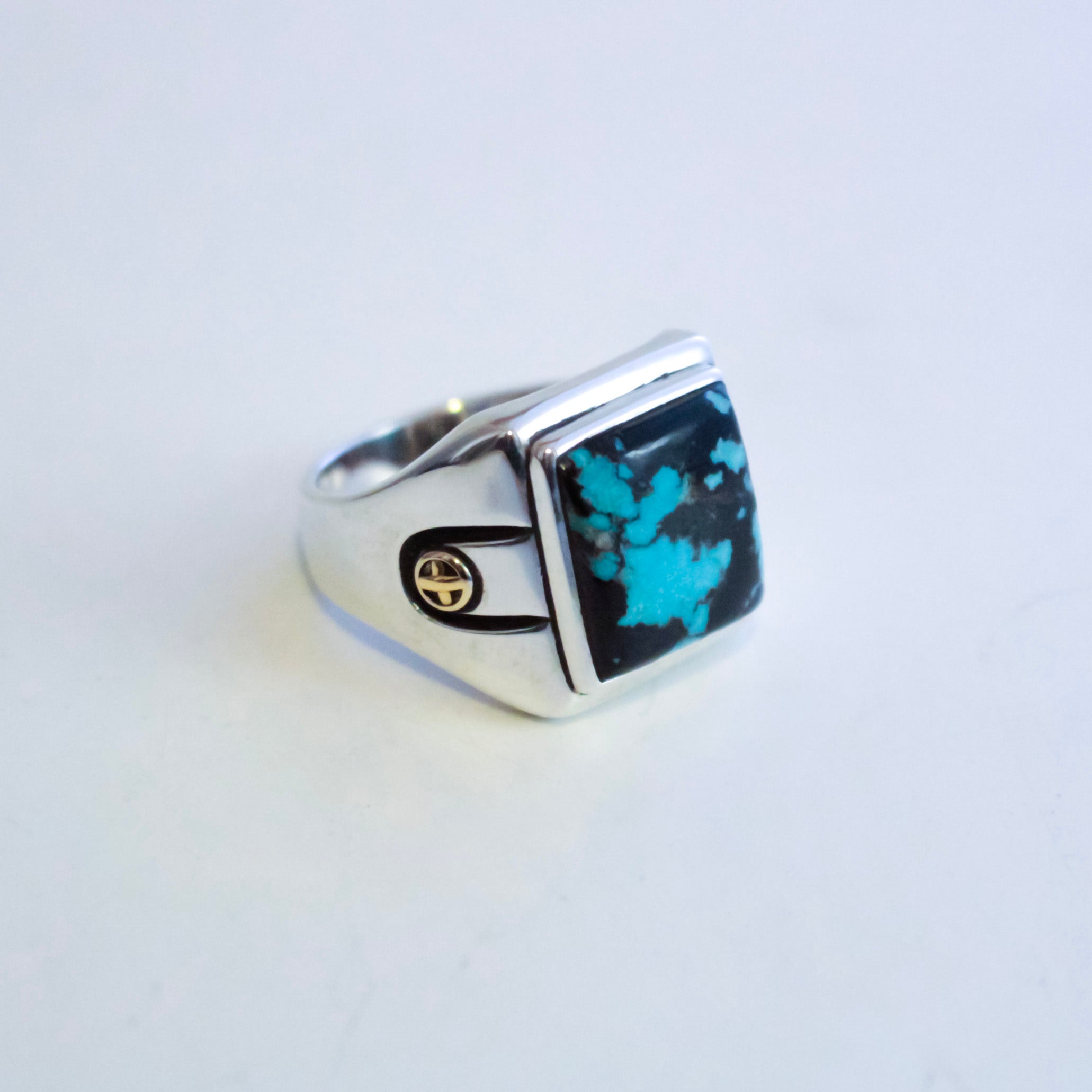 A silver signet ring featuring a square hubei turquoise stone, set against a plain light background.
