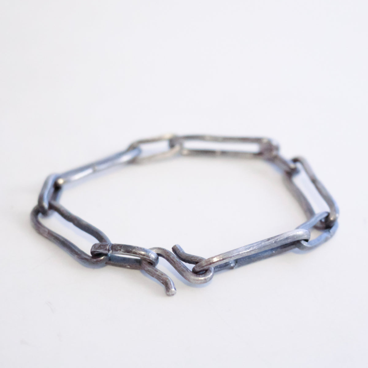 A handmade sterling silver chain link bracelet, featuring a rustic, weathered finish, displayed on a plain white surface.