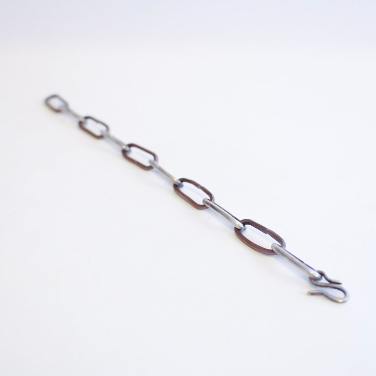 A sterling silver and copper chain bracelet with elongated oval links and a hook clasp, photographed diagonally on a plain white background.