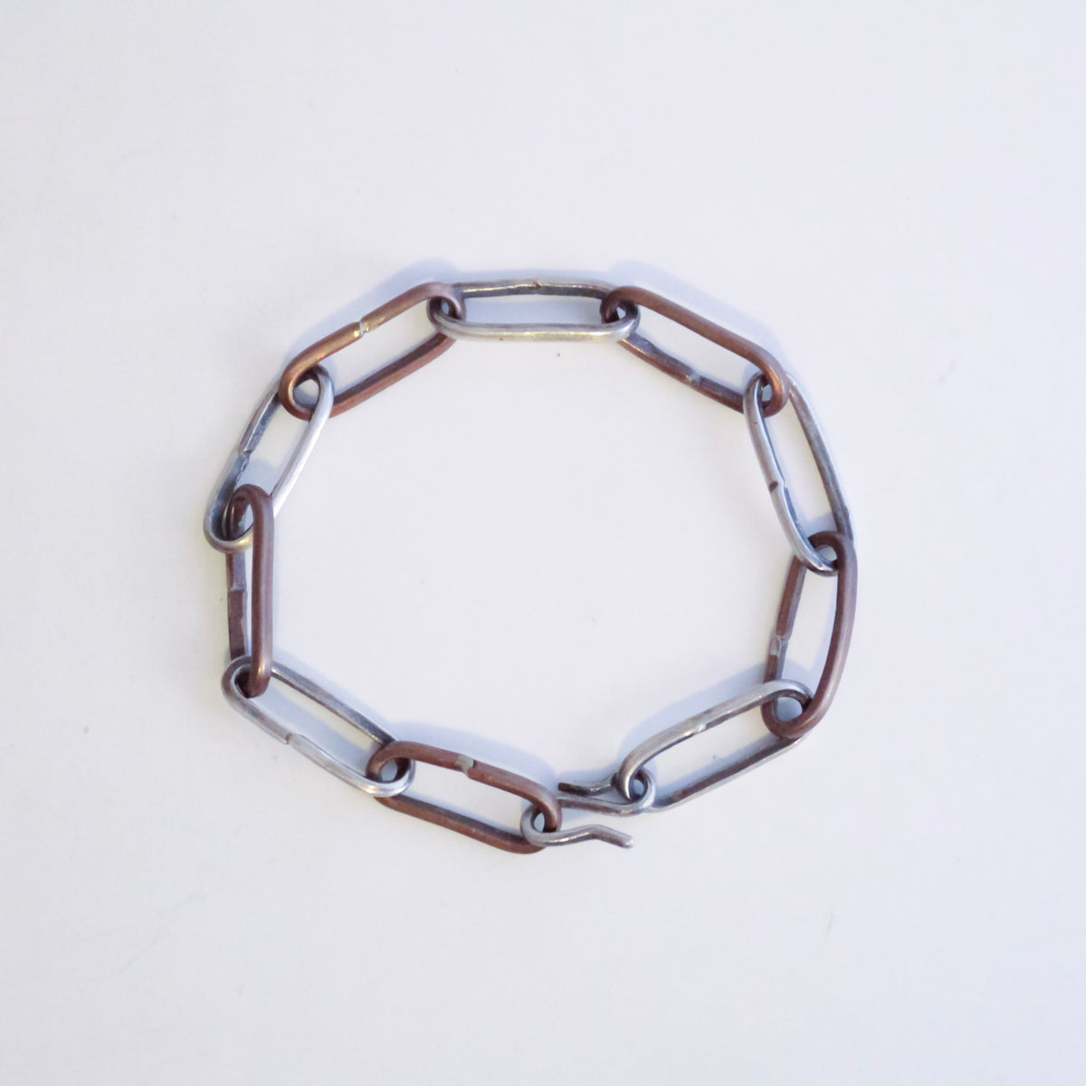 A sterling silver and copper chain bracelet with elongated oval links and a hook clasp, photographed diagonally on a plain white background.