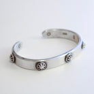 A silver-toned open cuff bracelet with five decorative starburst medallions spaced along the front, photographed on a plain light background.