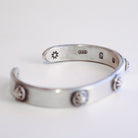 A sterling silver open cuff bracelet with decorative circular and triangular bezel-set details, photographed on a clean white background.