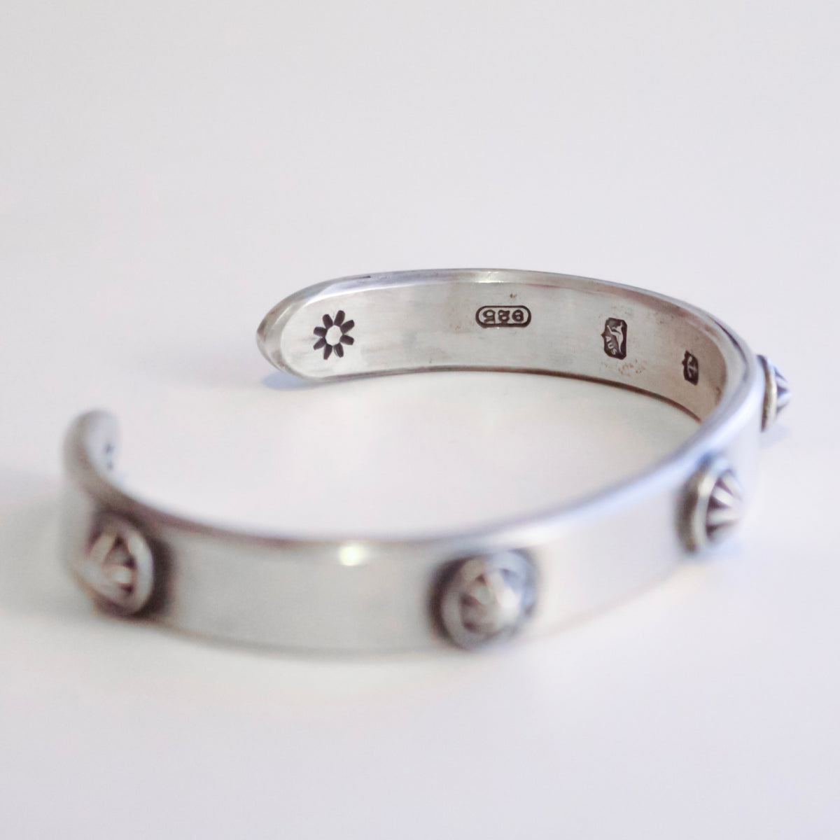 A sterling silver open cuff bracelet with decorative circular and triangular bezel-set details, photographed on a clean white background.
