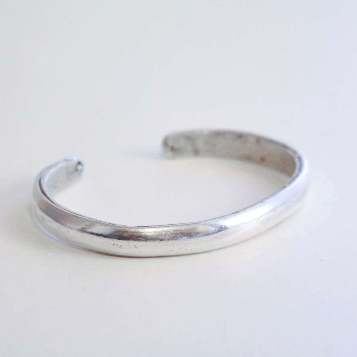 A polished silver cuff with a polished finish and a textured interior, shown on a plain white background.