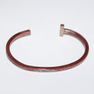 A hammered copper-toned open cuff with a small rectangular accent at the open end, shown on a plain white background.