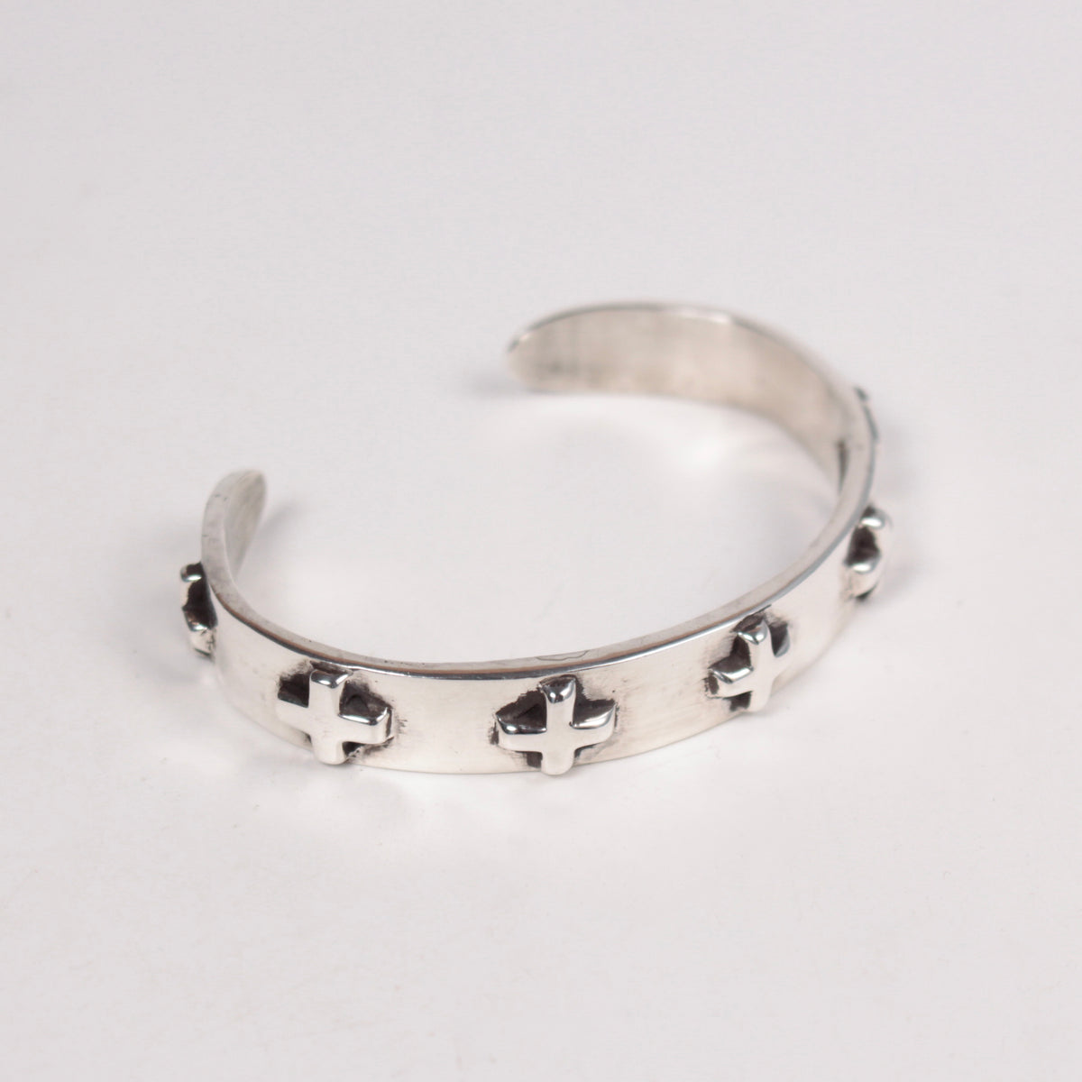 A silver open cuff bracelet featuring small raised cross star motifs spaced along the front, photographed on a plain light background.