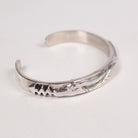 A polished sterling silver cuff bracelet with hand-carved serpent details on a plain white background.