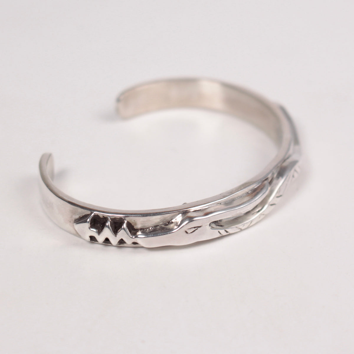 A polished sterling silver cuff bracelet with hand-carved serpent details on a plain white background.