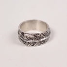 A sterling silver feather band ring with detailed feather textures, photographed on a plain light background.