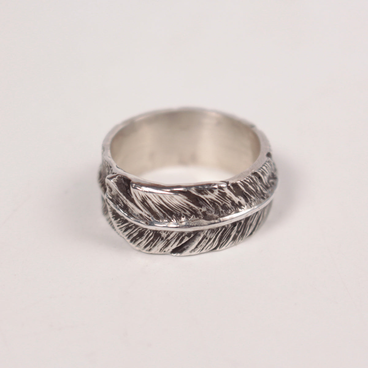 A sterling silver feather band ring with detailed feather textures, photographed on a plain light background.