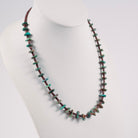 A beaded necklace displayed on a white mannequin bust. The necklace features small, irregular turquoise stone chips spaced by smaller pin shell beads. 