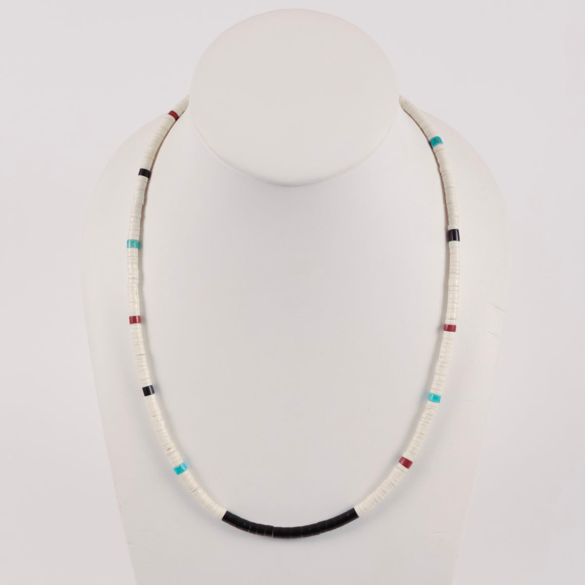 A beaded necklace displayed on a white mannequin bust against a light gray background. The necklace consists of predominantly white beads with small accent beads in turquoise blue, black, red, and white.